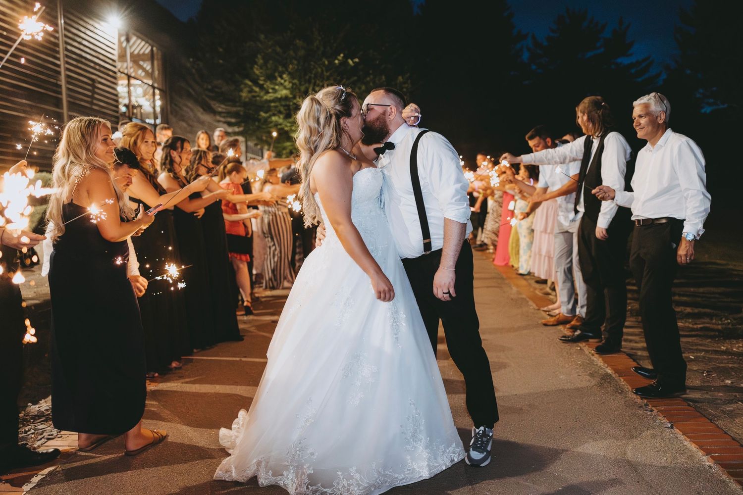 Wedding party exit with guests holding sparklers creating a glowing pathway at night.