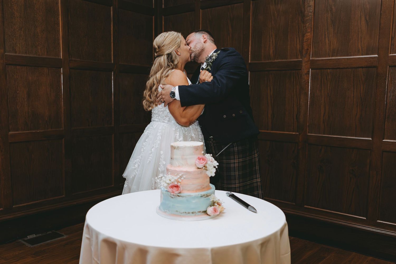 A couple shares their first dance at a wedding reception in a wood-paneled venue.