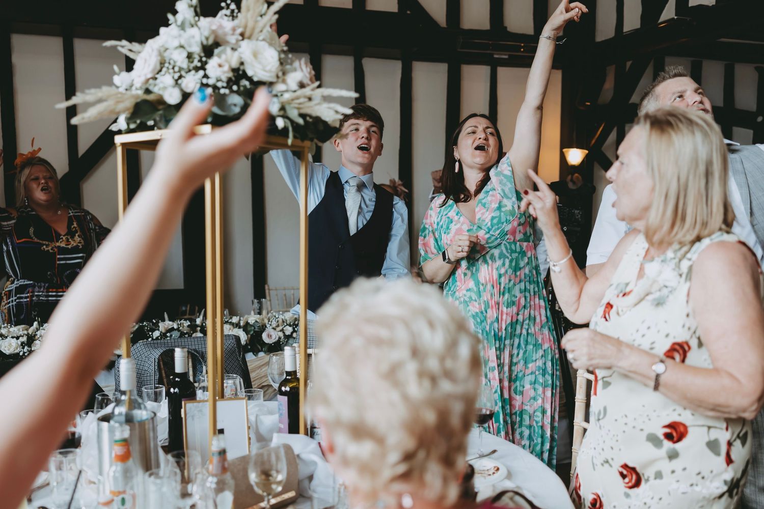 Wedding guests in colorful dresses dance and celebrate at an indoor reception.