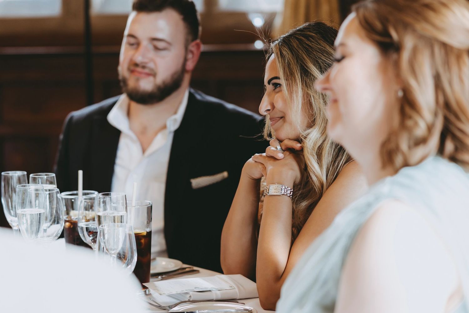 Wedding reception guests enjoying speeches in an elegant dining room setting.