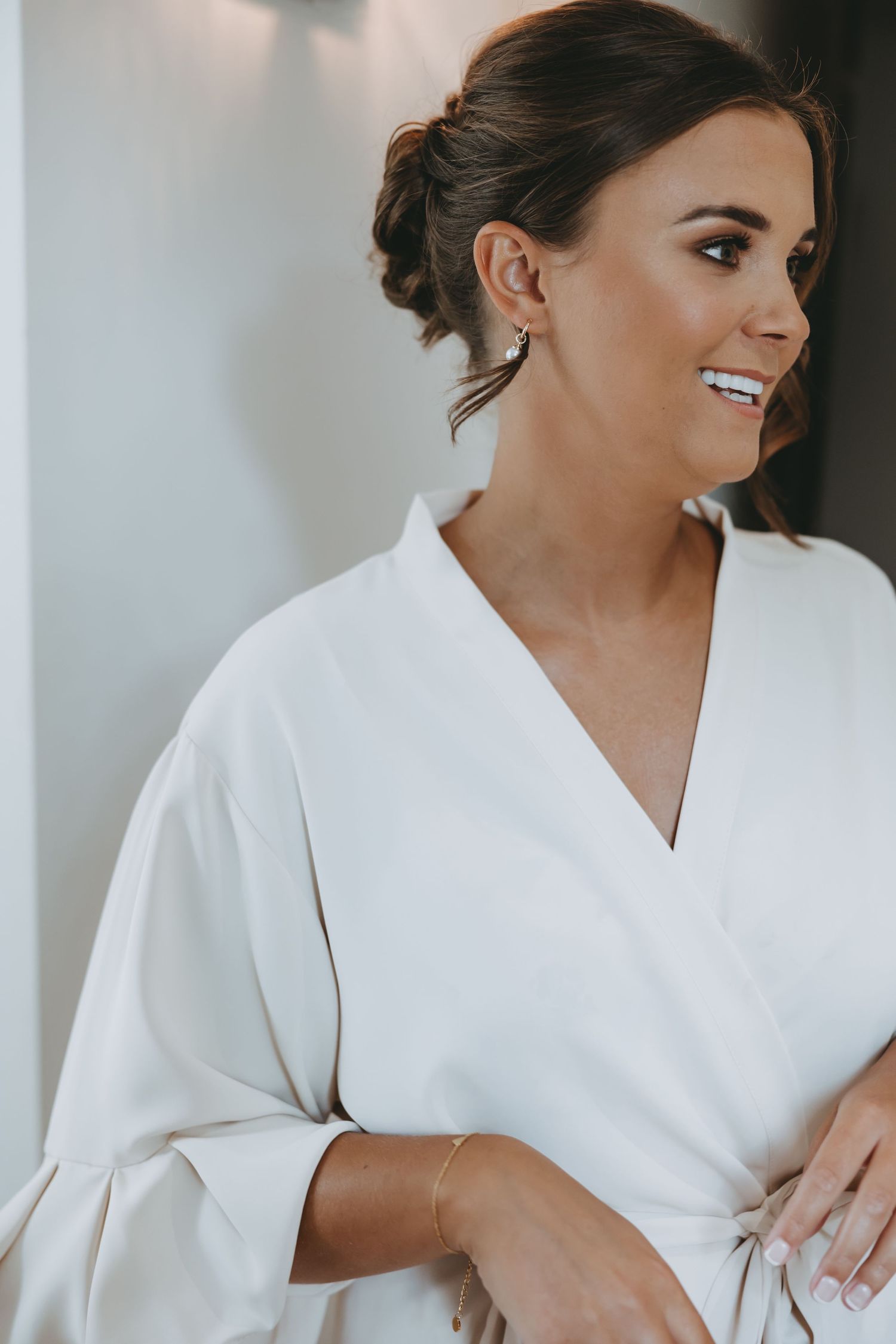 Woman wearing white silk robe during wedding morning preparations.