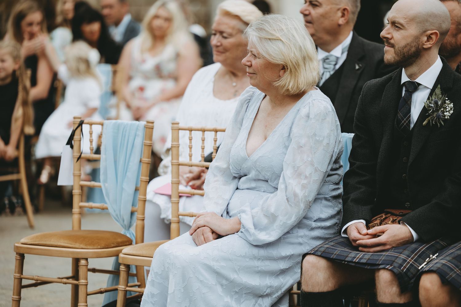 Wedding guests seated on elegant wooden chairs at an outdoor ceremony.