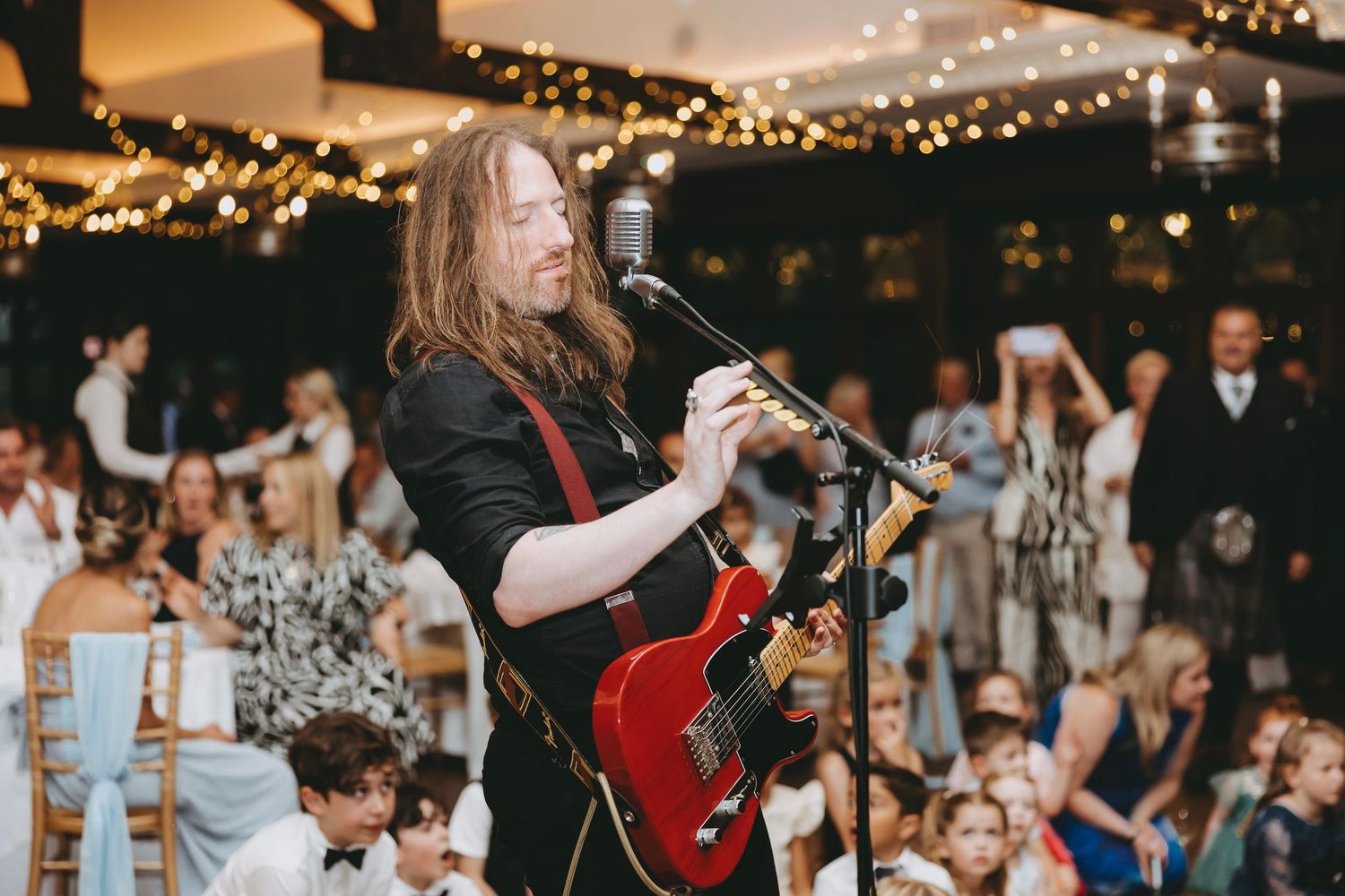 Wedding reception venue decorated with warm string lights and featuring live music entertainment.