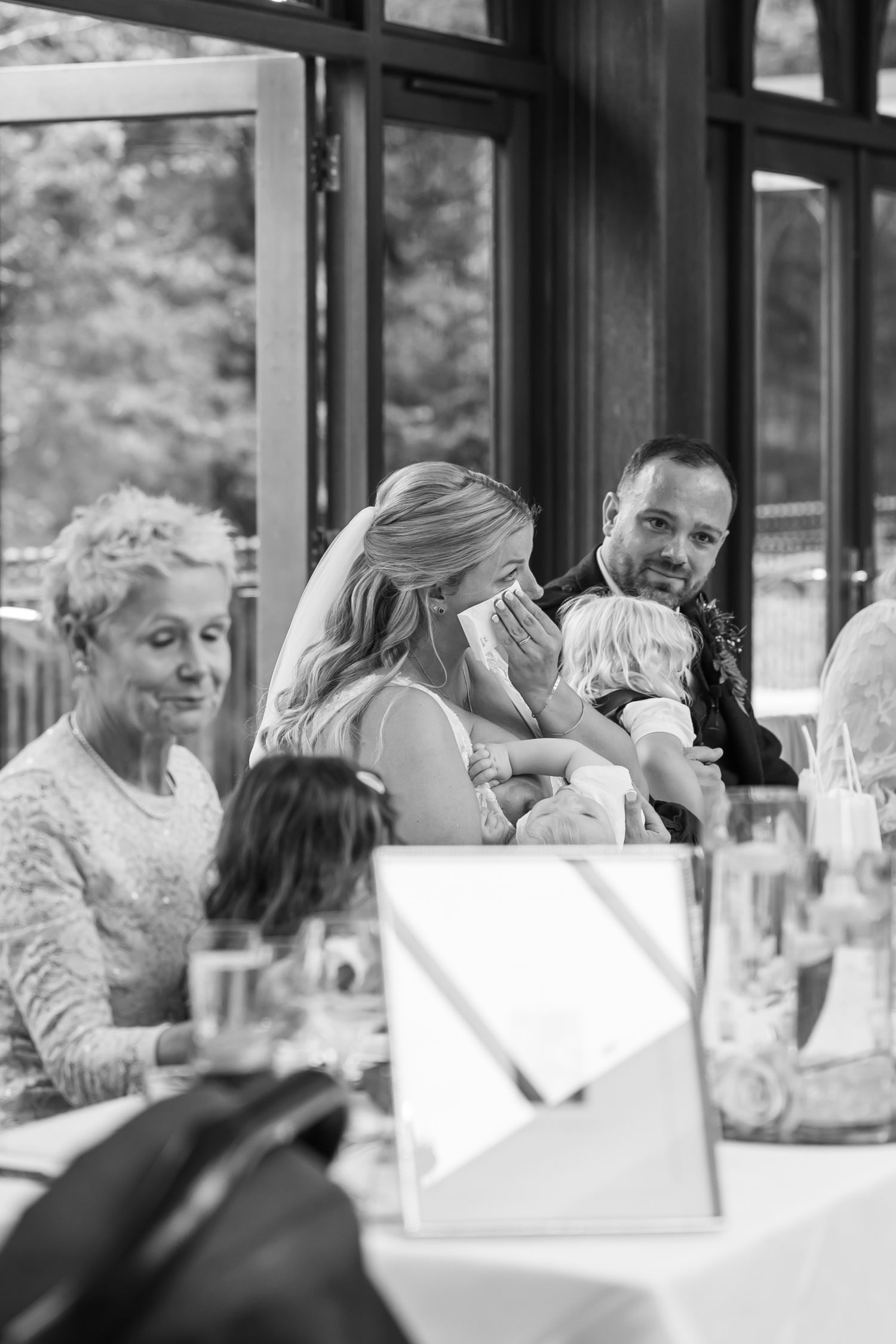 Black and white candid shot of wedding reception guests at decorated dining tables.