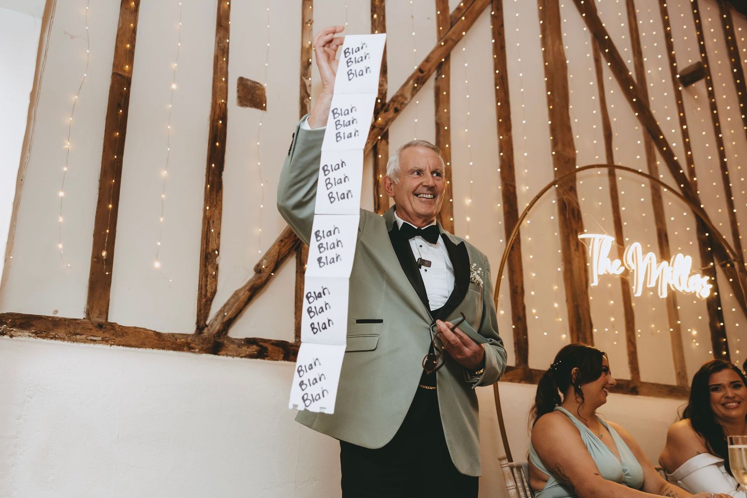 Wedding reception venue with exposed wooden beams decorated with fairy lights and white signs.