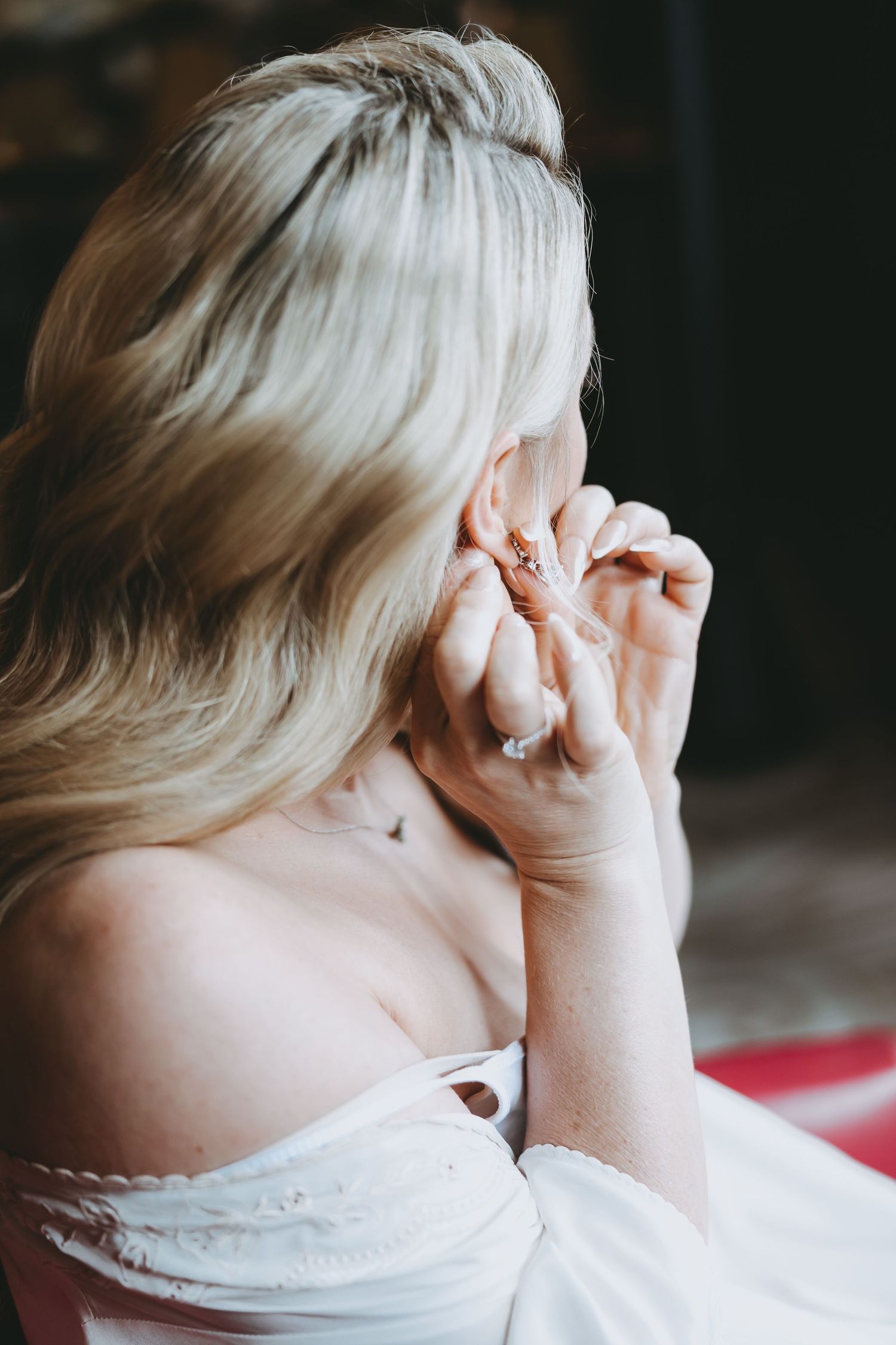 Side view of person with blonde hair covering face with hands in dramatic lighting.