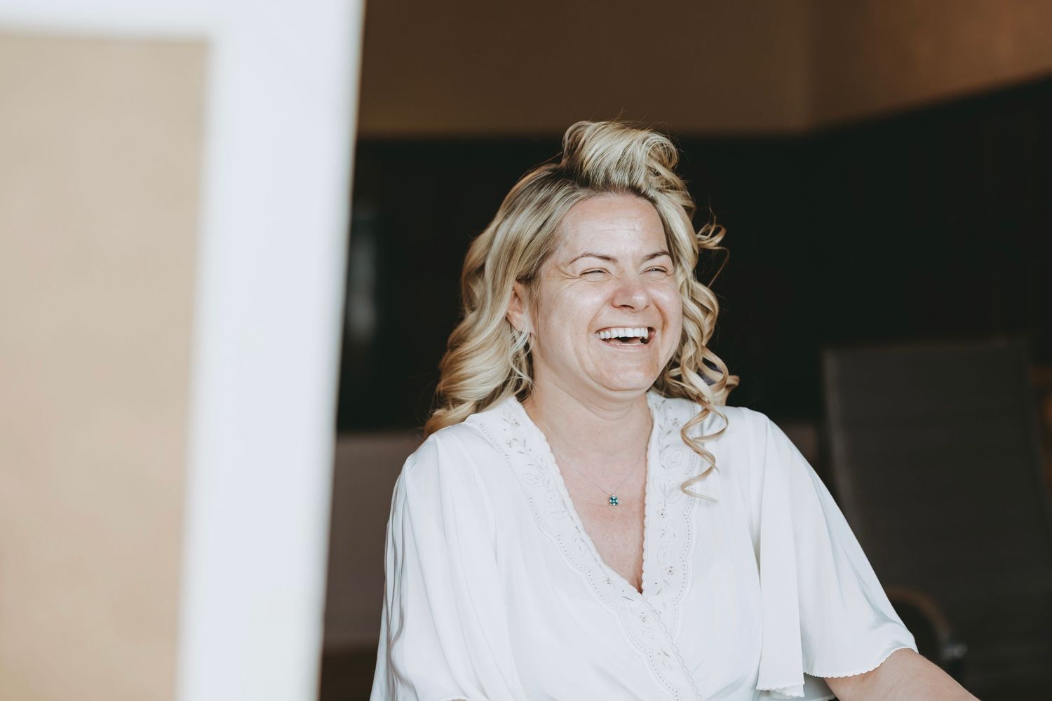 Someone in a white robe smiling during their makeup application session.