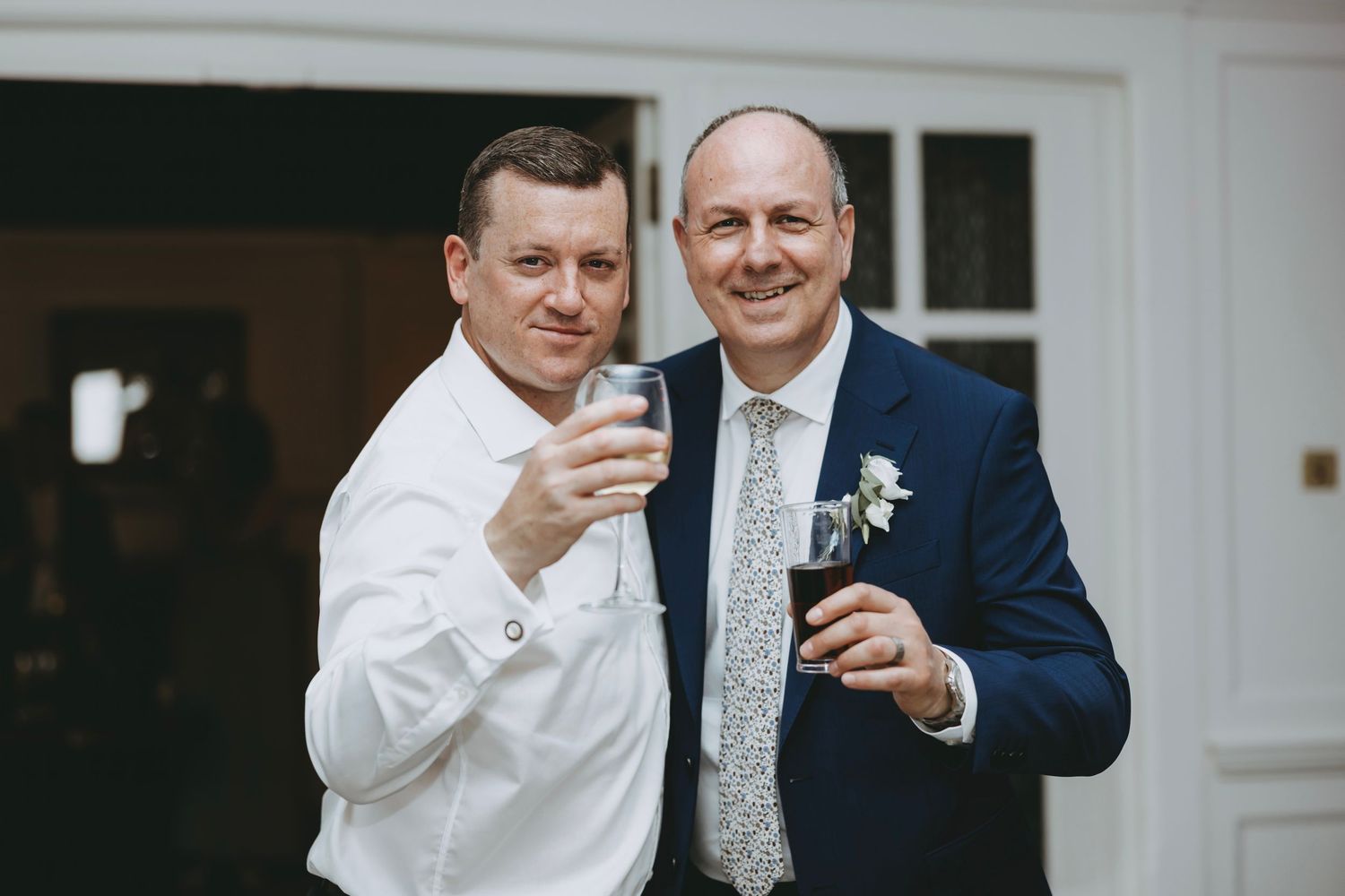 Wedding guests interacting during reception in formal attire against white walls.