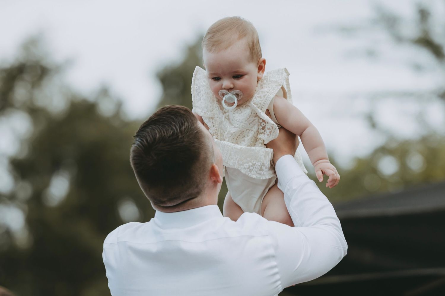 Parent lifts baby during outdoor wedding celebration.