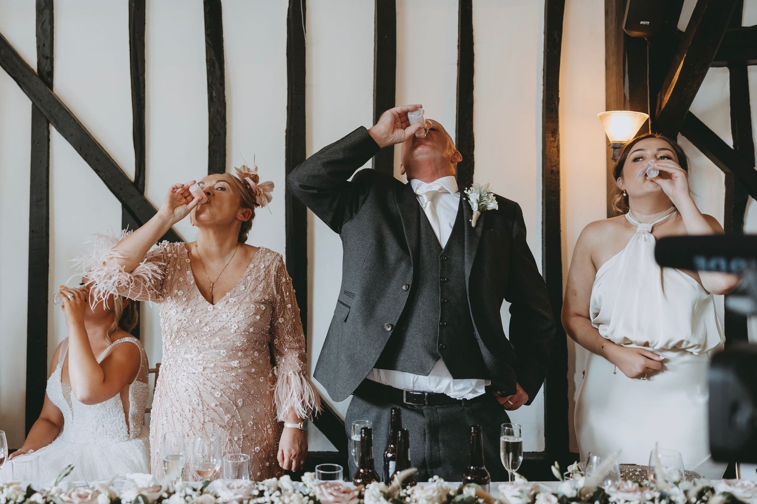 Wedding reception guests share emotional reactions during speeches in timber-framed venue.