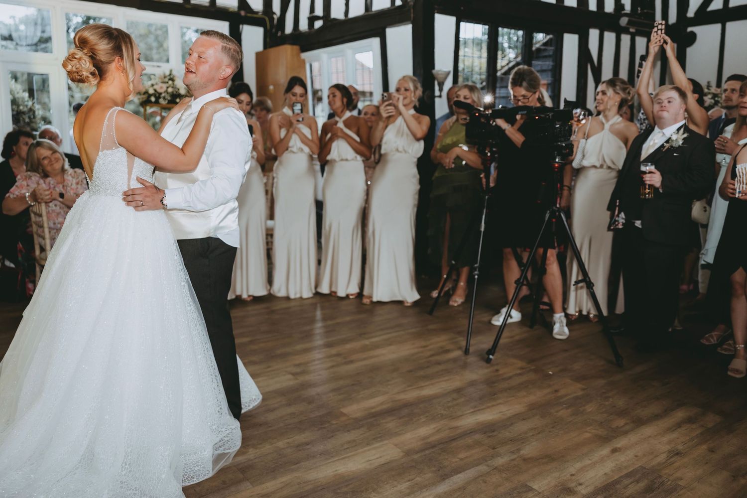 Wide shot of wedding reception showing guests watching couple's dance in Tudor-style venue.