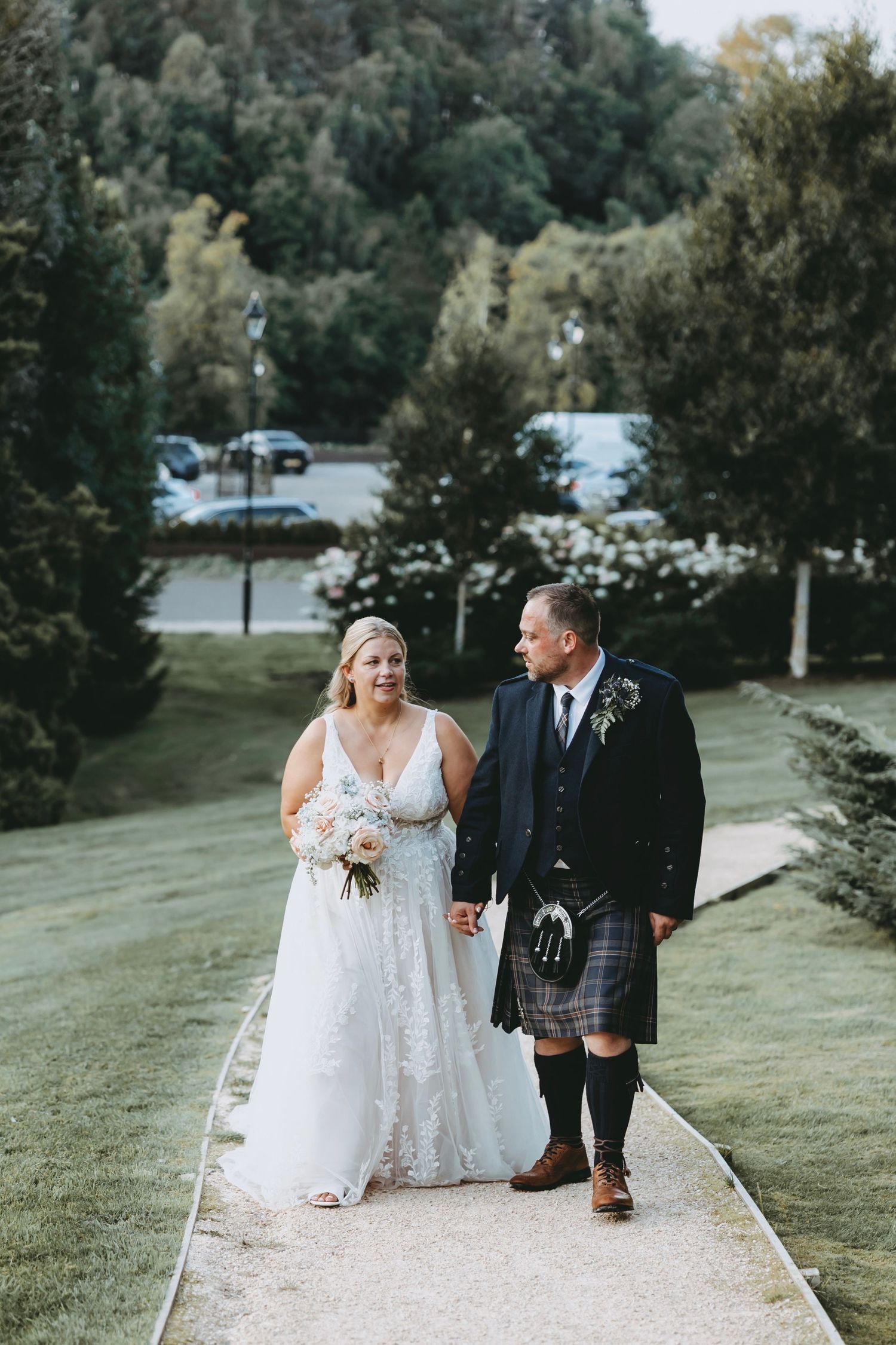 Newlyweds sharing a romantic moment on a grassy hillside path.