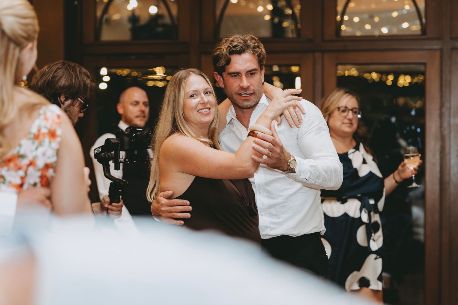 Wedding guests celebrate on the dance floor under string lights at an evening reception.