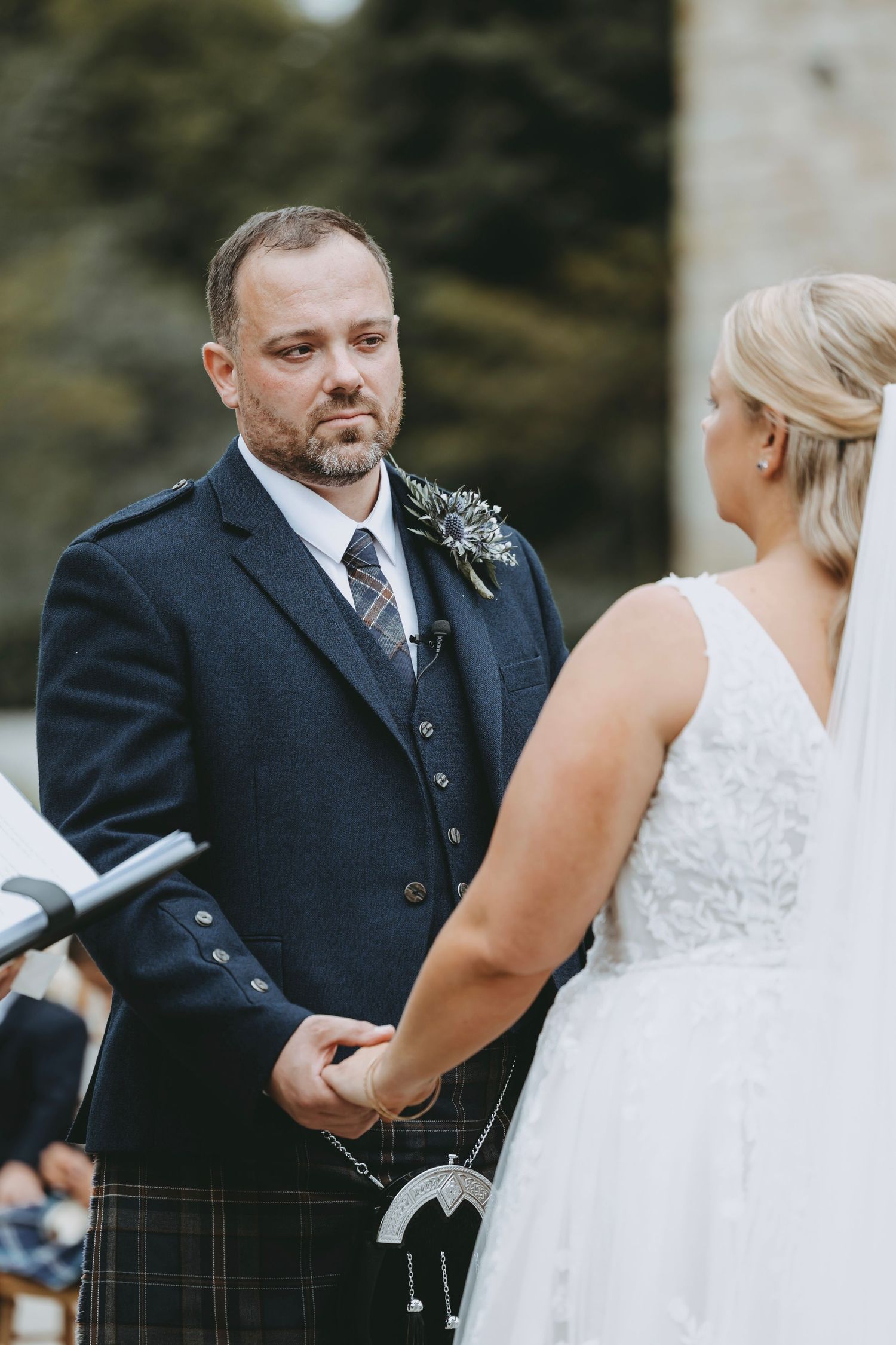 Close-up of wedding ceremony participants in Scottish formal wear exchanging vows.