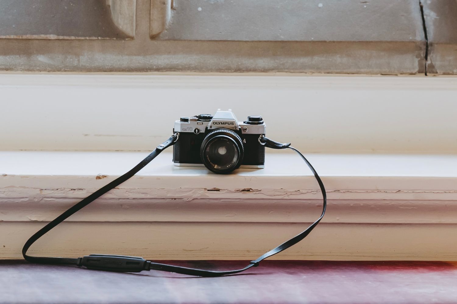 A vintage camera sits on a white windowsill next to a window frame and decorative trim.