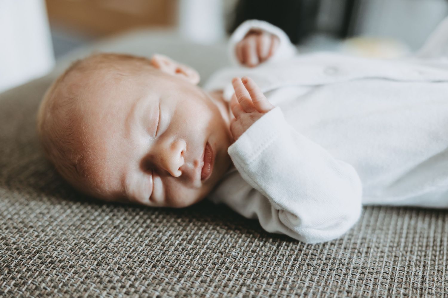 A sleeping newborn baby wrapped in white swaddling blankets lies peacefully on a textured gray surface.