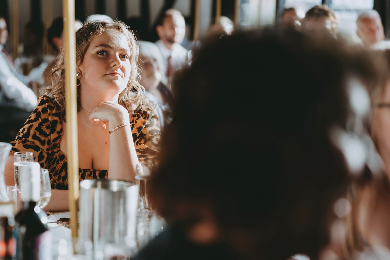 Wedding guests listen attentively during reception speeches in rustic timber-framed hall.
