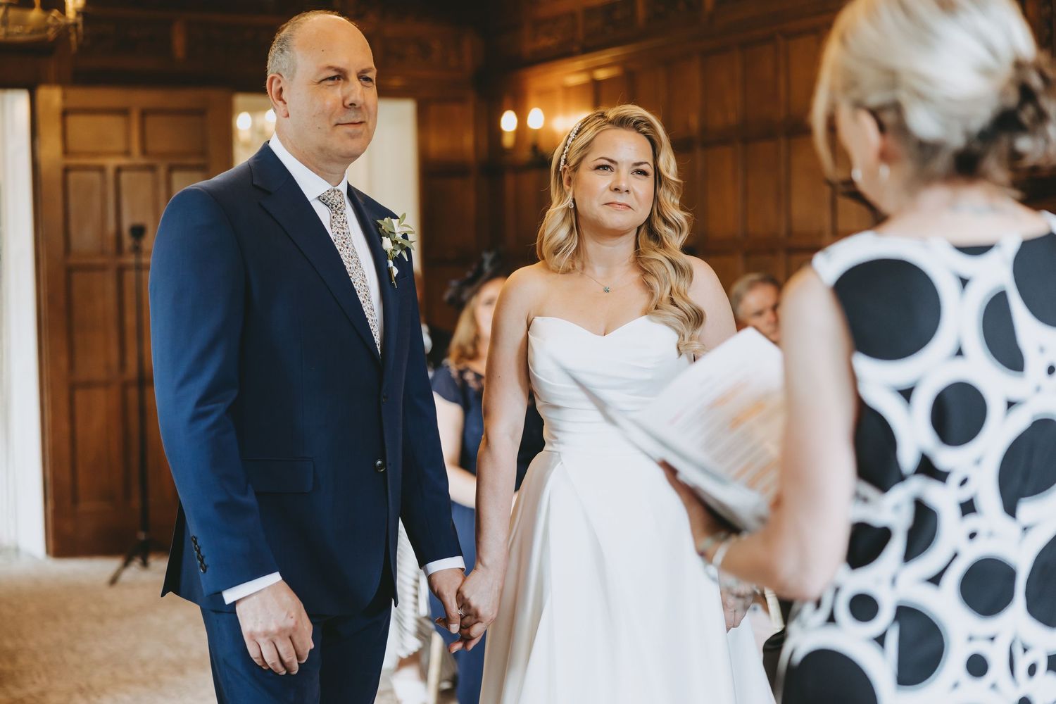Wedding party members sharing candid moments in a wood-paneled room with elegant decor at Fanhams Hall, Ware, Hertfordshire.