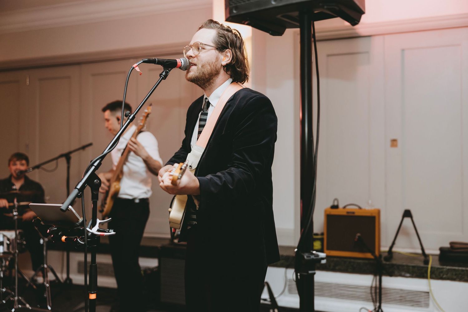 Musicians perform on stage at a wedding reception with saxophone, guitar and microphone setup in an elegant venue.