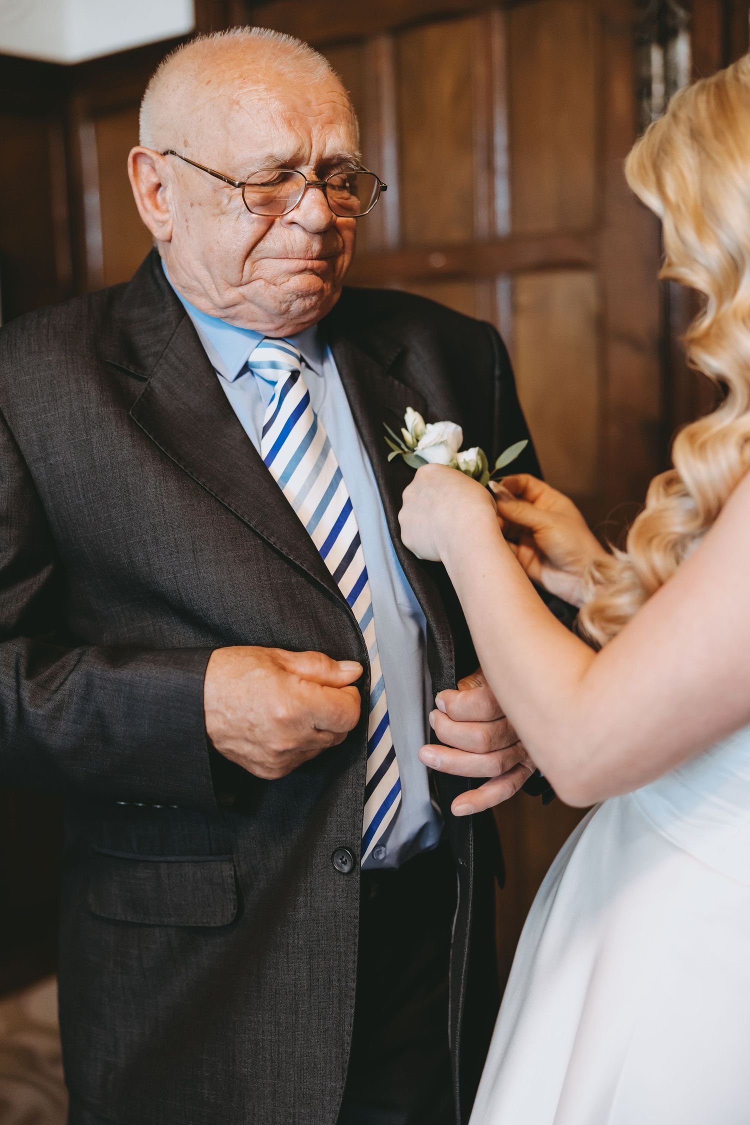 Candid moment of a bride attaching a white boutonniere to an elderly man's suit.
