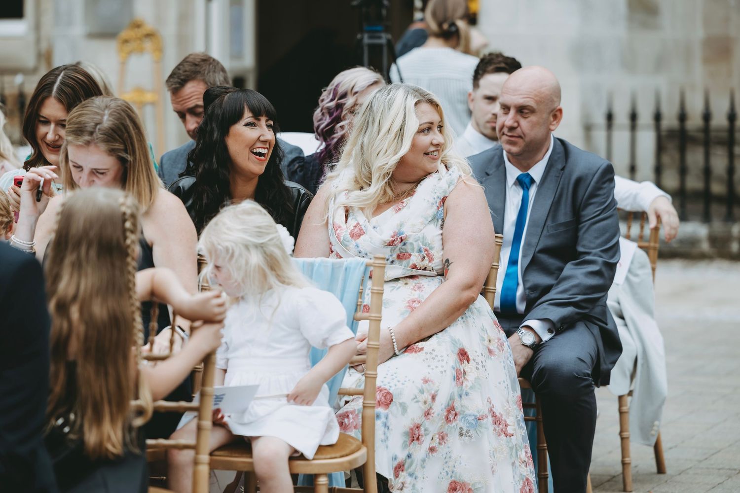 Outdoor wedding reception with guests seated in wooden chairs.
