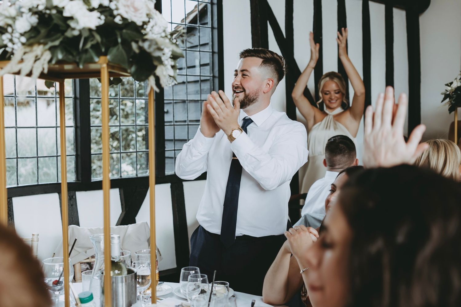 Guests celebrate with raised glasses in an elegant venue with black and white timber decor.