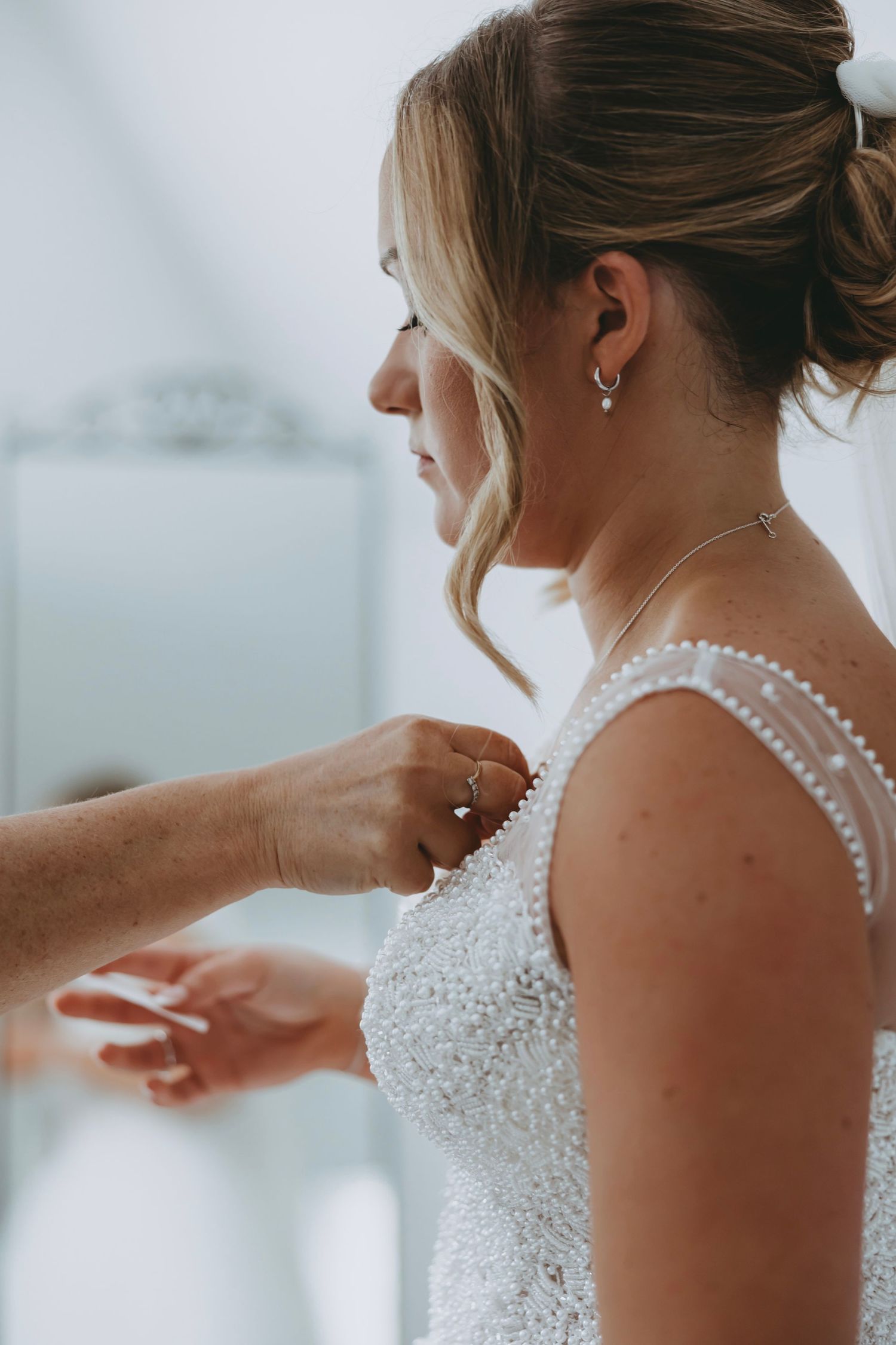Detail shot of hands adjusting the beaded strap of a white wedding dress.