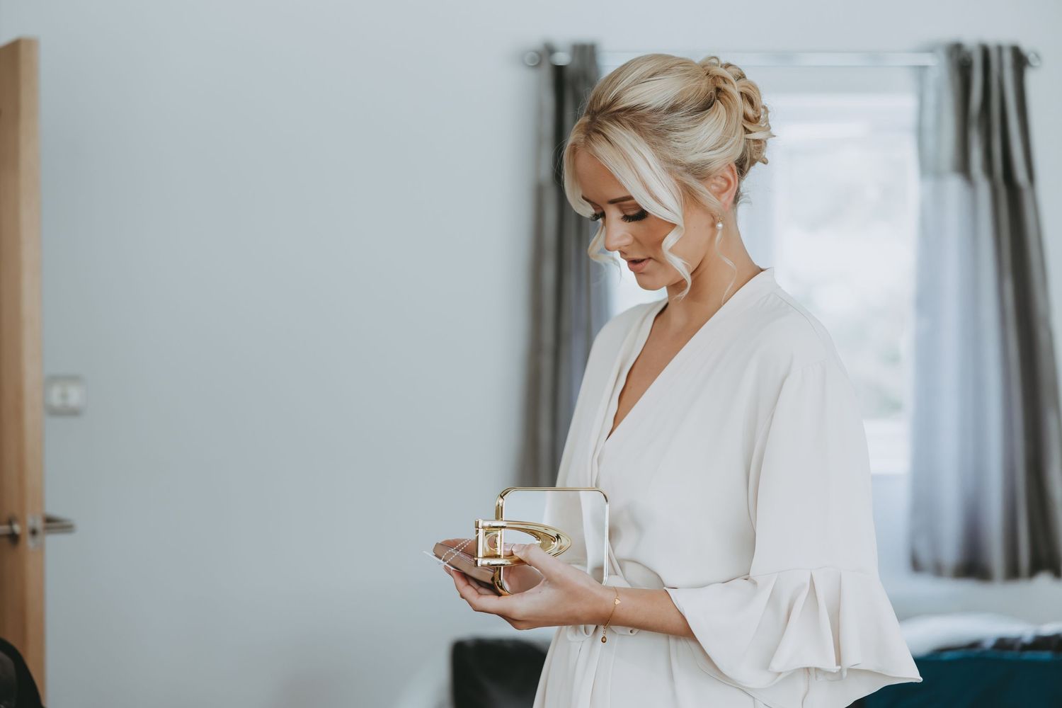 Woman in white robe checking her phone during wedding preparations.