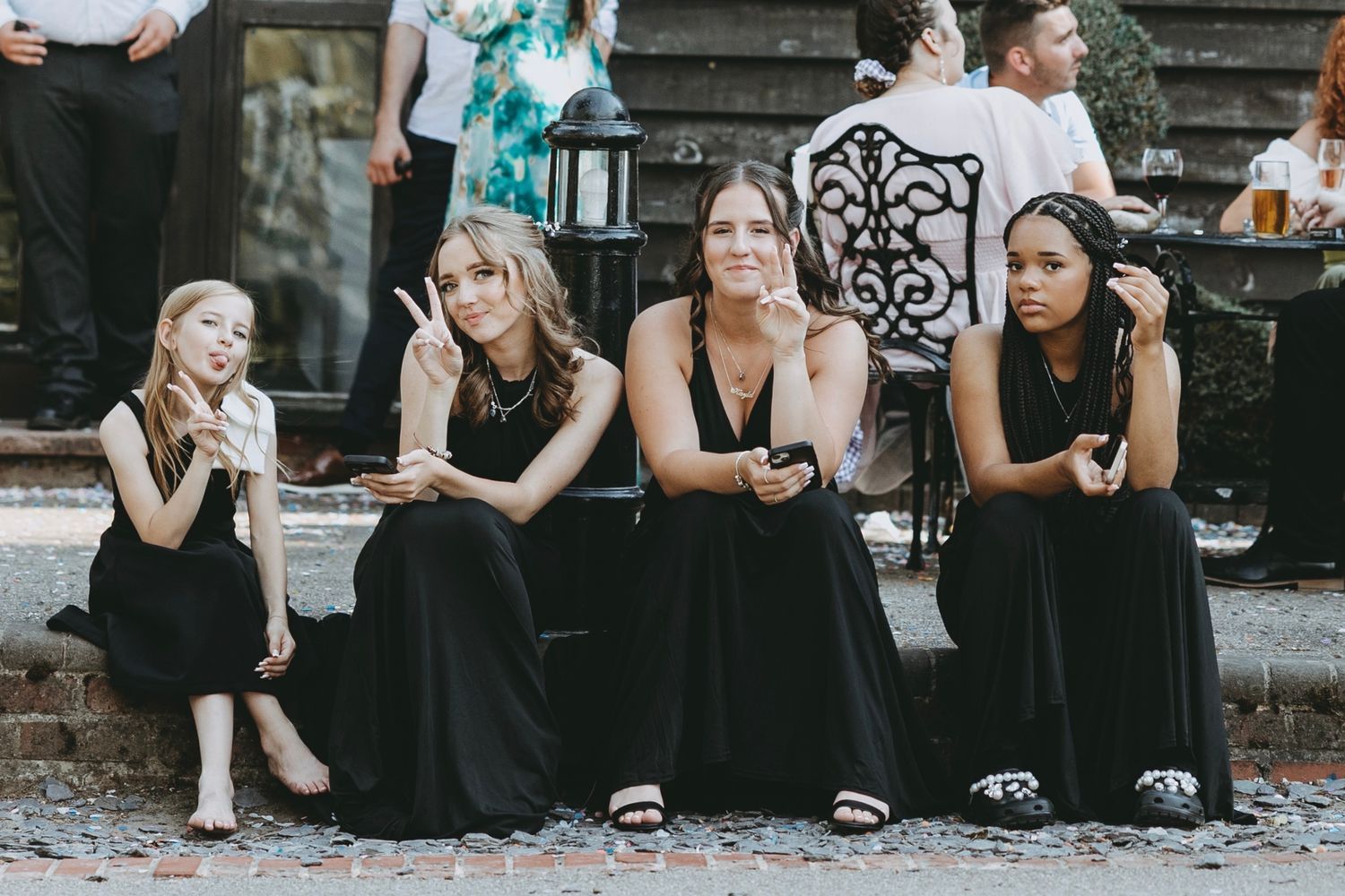 Wedding party members in black dresses sitting on outdoor stone steps.