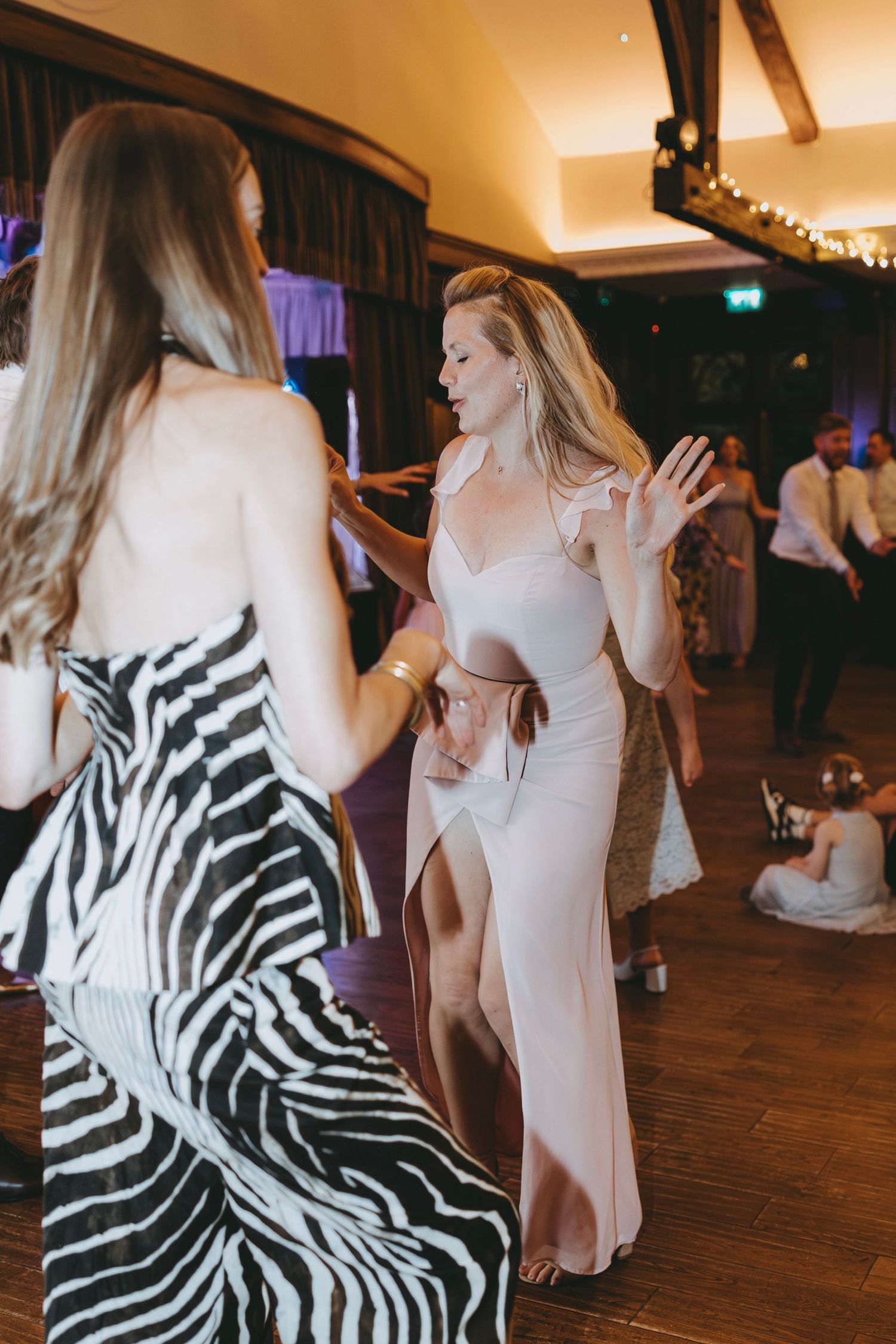 Wedding guests dance on wooden floor with zebra print and white dresses visible.