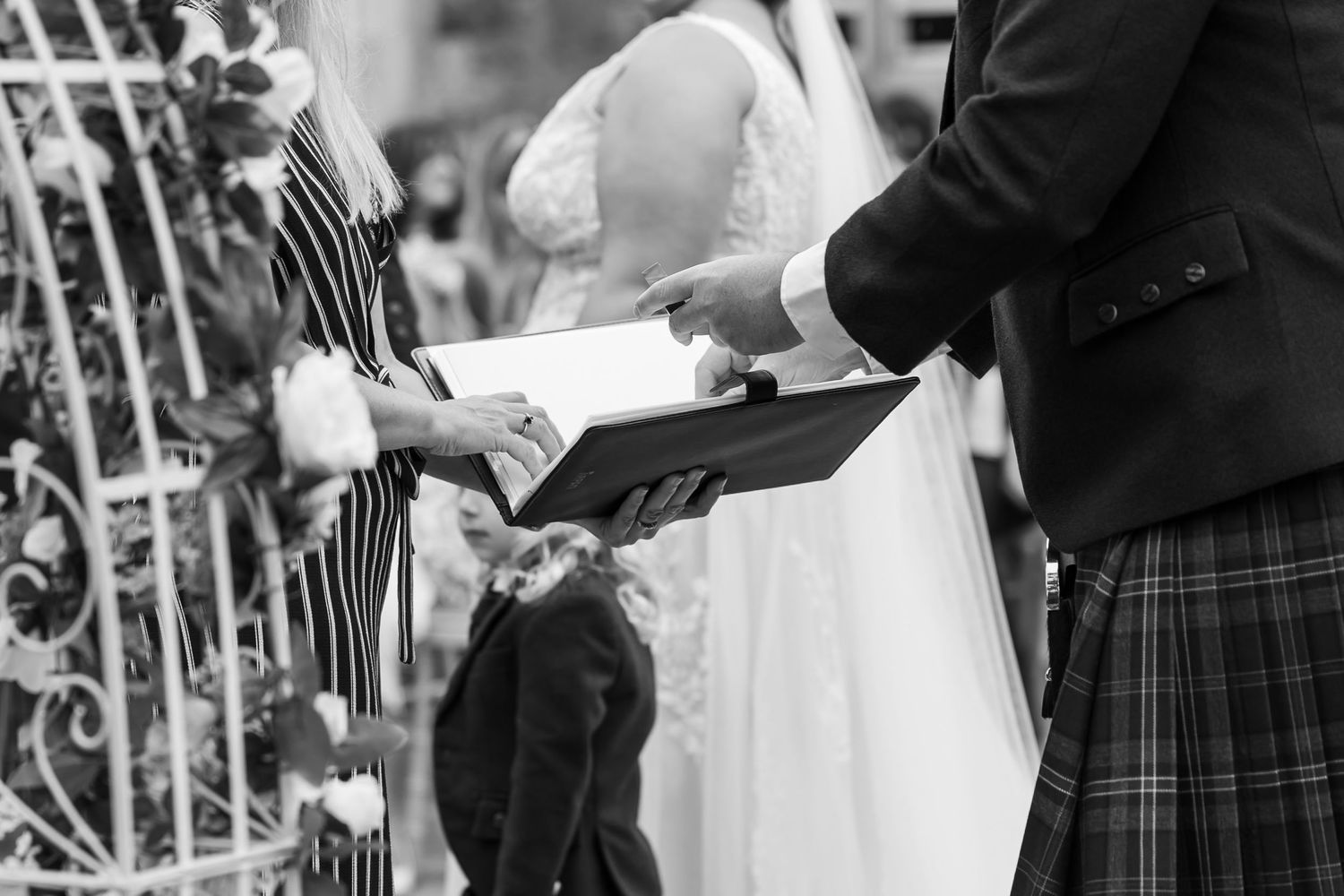 Wedding ceremony detail showing traditional Scottish attire and white floral decorations.