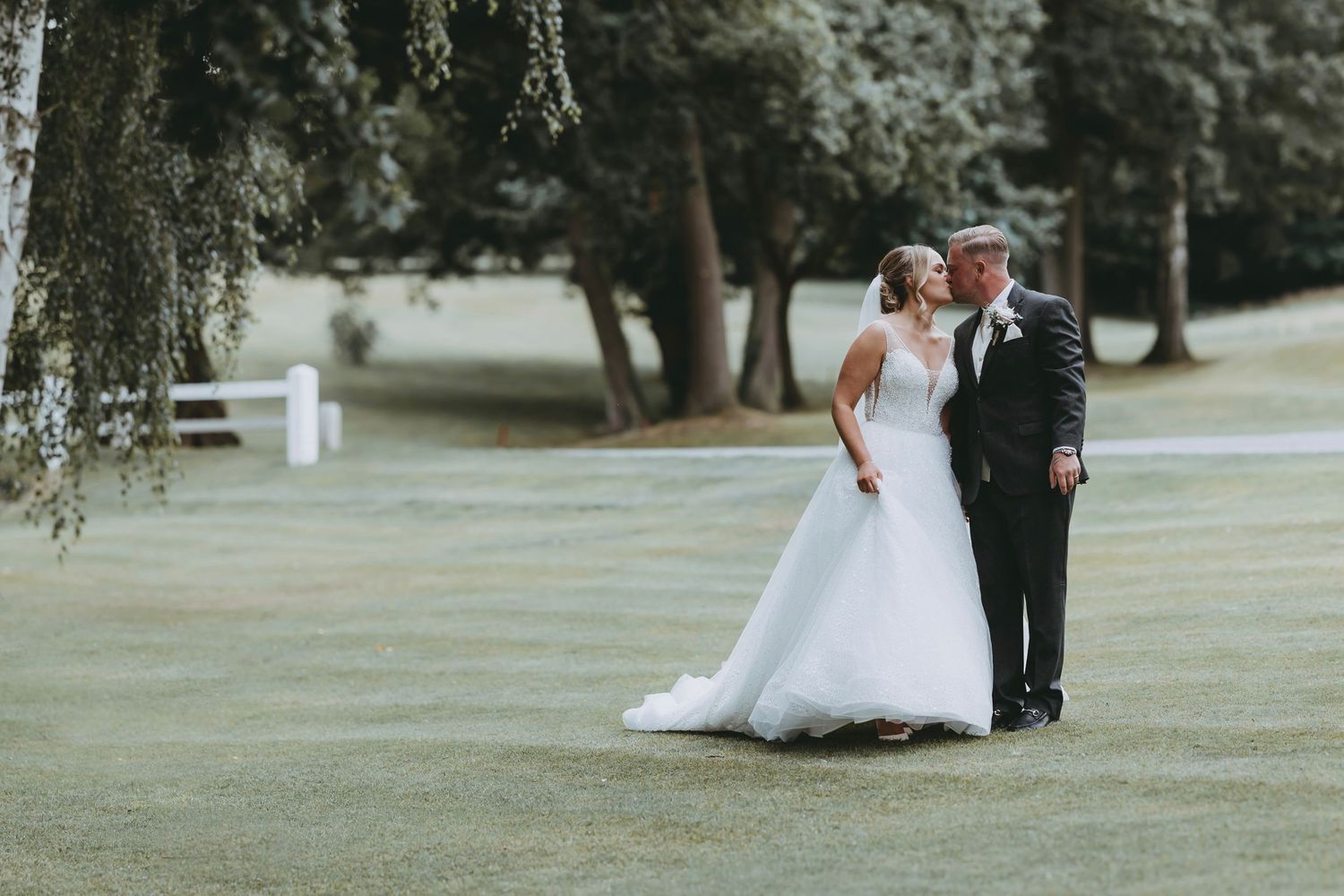 Wide landscape shot of newlyweds strolling across an expansive grass lawn on their wedding day.