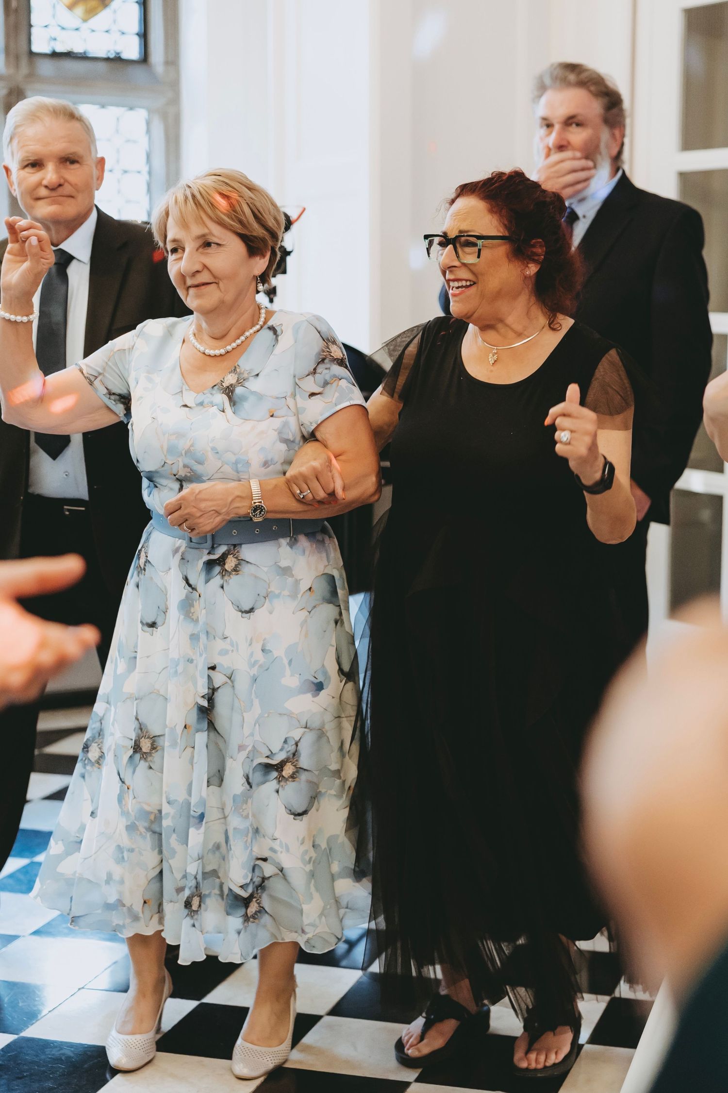 Guests in formal attire dance and smile during a lively wedding reception celebration.