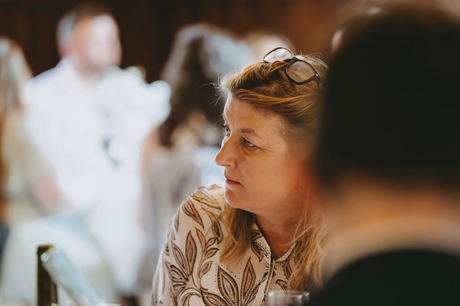 Attendees socializing at an indoor gathering with elegant table settings and dark wood walls.