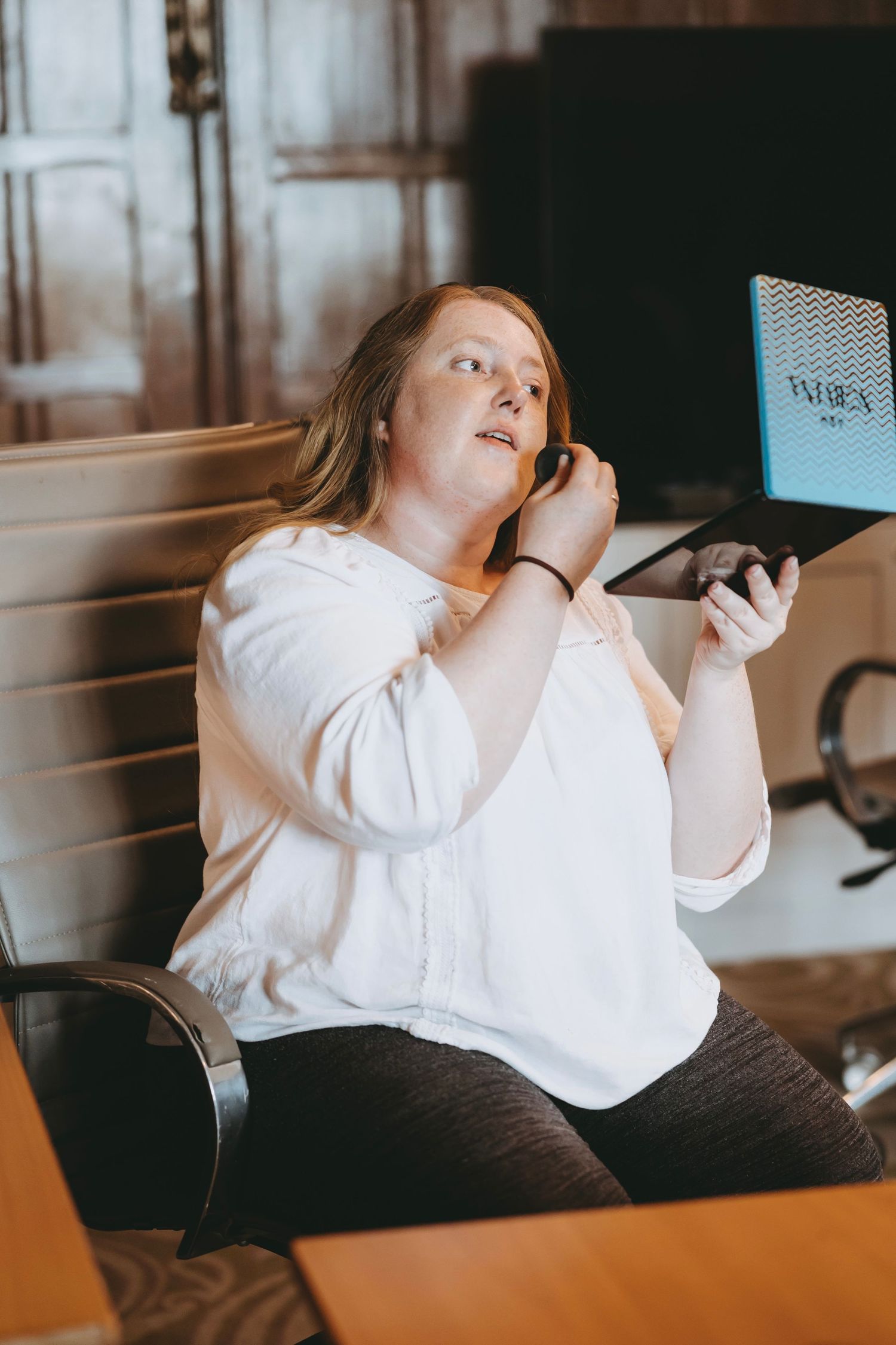 Person in white blouse looking at phone while sitting in office setting.