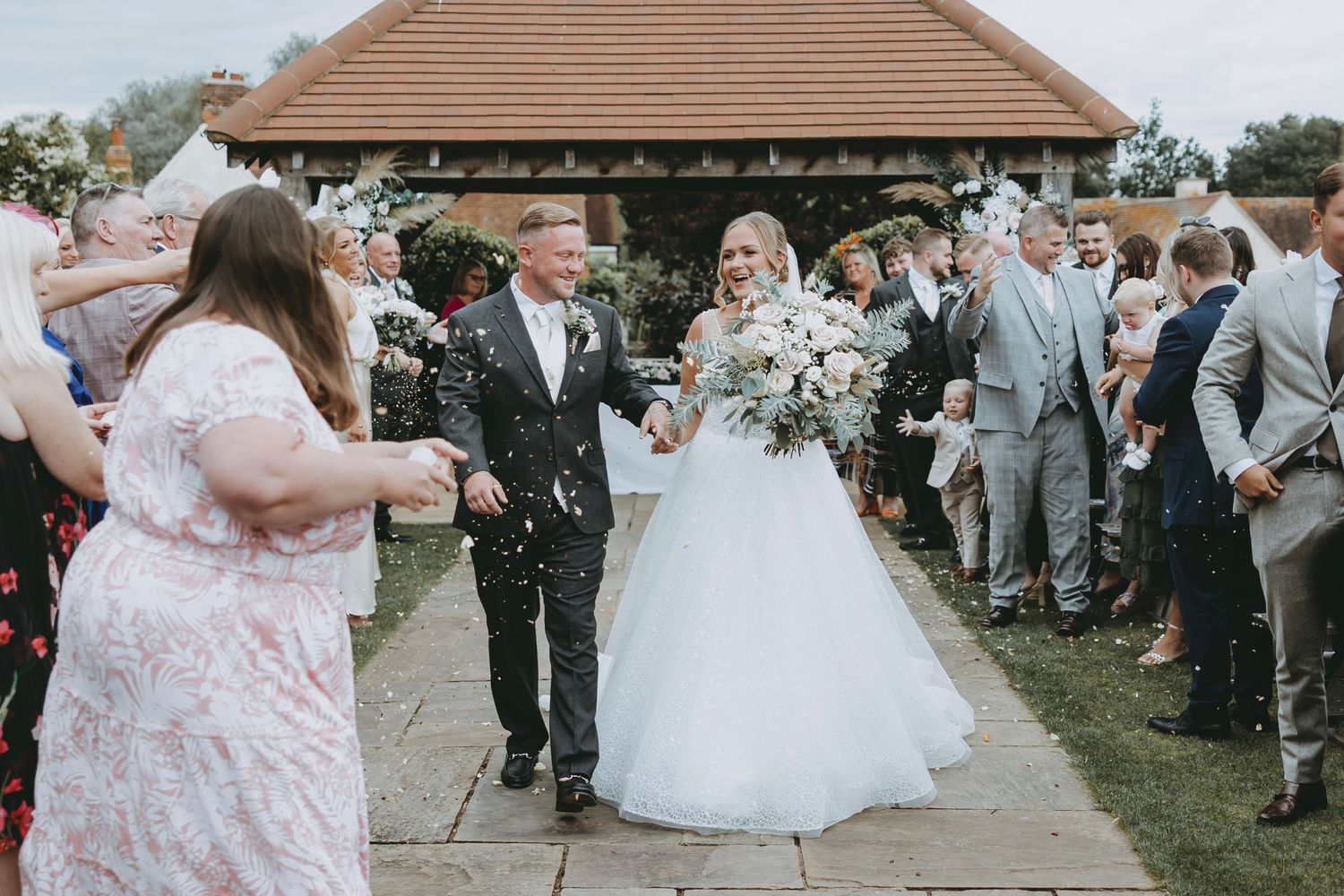Guests celebrate at an outdoor wedding venue with confetti and floral decorations.