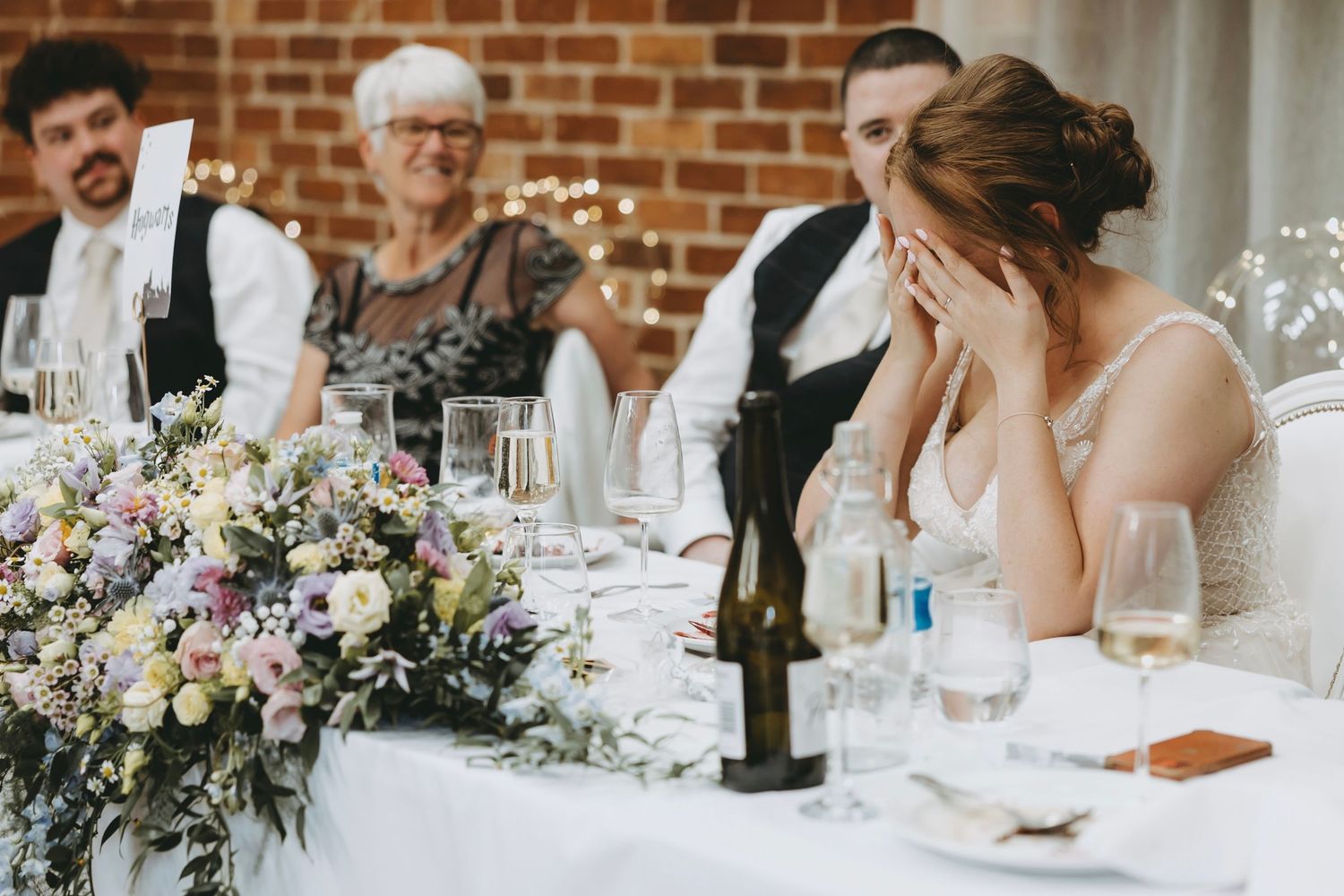 Wedding reception guests sharing emotional moments at tables with exposed brick backdrop.