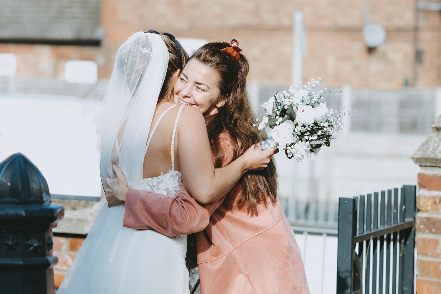 A bride shares an emotional embrace with a guest in a peach dress.