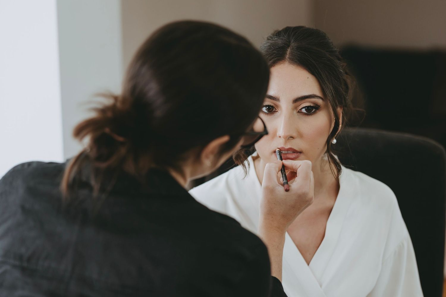 Bride getting ready with bridesmaids in white robes during wedding morning preparations.