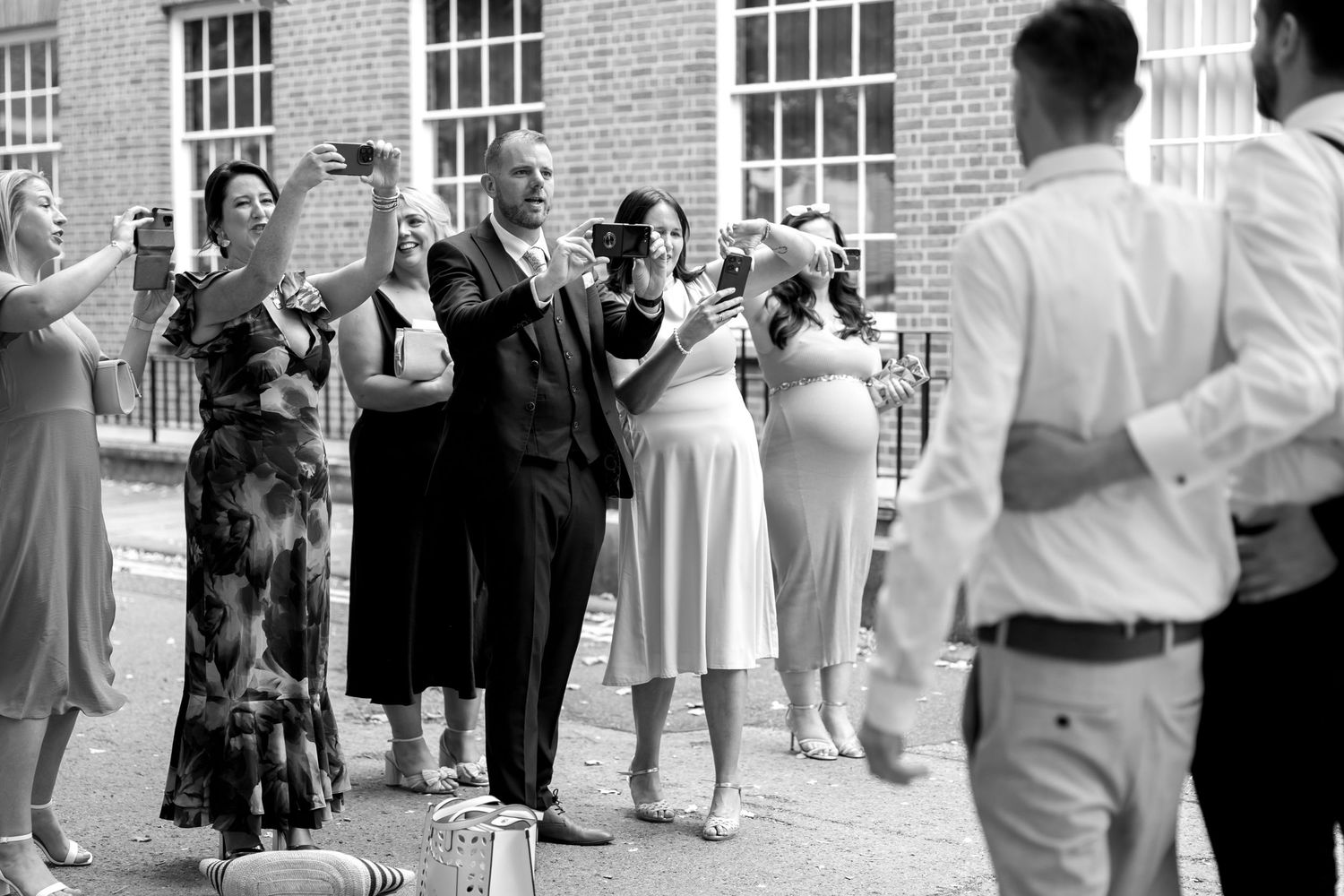 Wedding guests mingle outside historic brick building during reception.