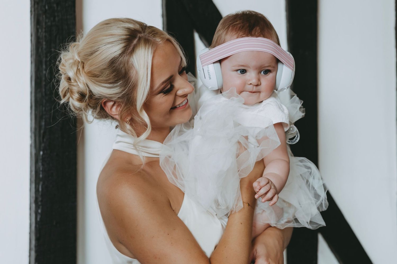 Baby in white christening dress being held during a celebration.