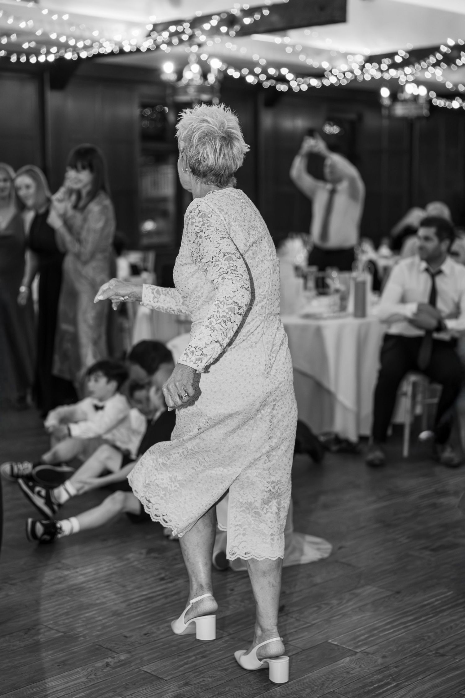 Little ones in white dresses dance playfully on a wooden dance floor at a wedding reception.