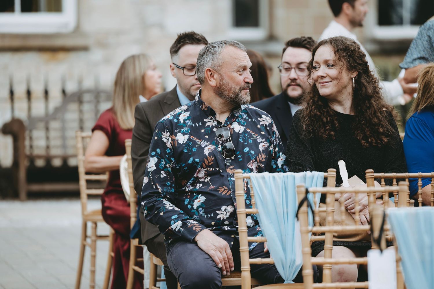 Guests seated in rows of wooden chairs at an outdoor event venue.