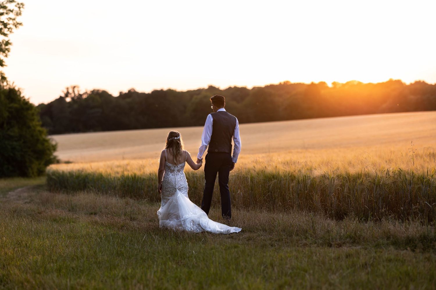 Wedding couple silhouetted against dramatic sunset in rural field.