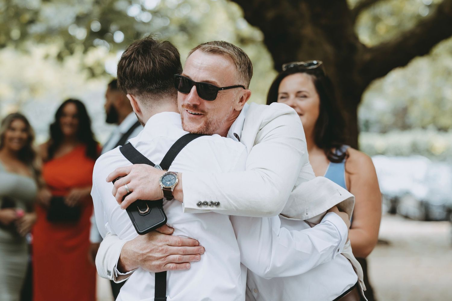 Wedding party members embrace during outdoor celebration photos.