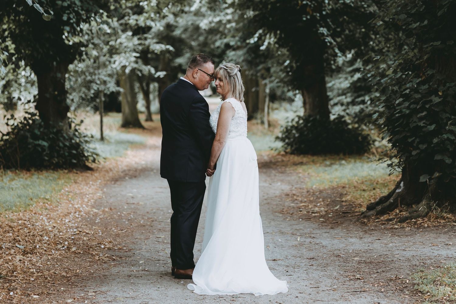 Bride and groom walking together on a tree-lined path during an autumn wedding photoshoot.