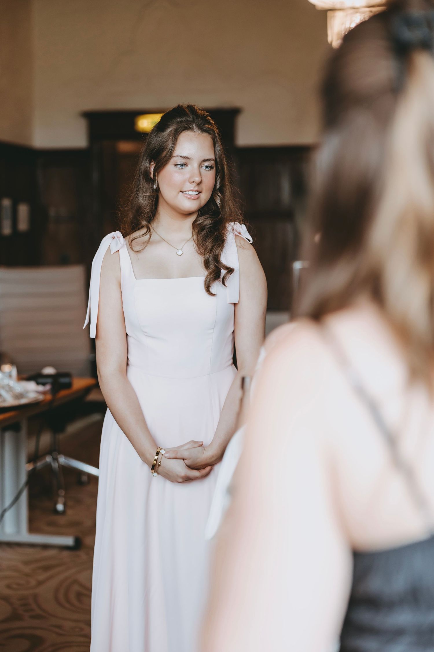 People in white dresses and formal wear interact in an elegant indoor space.