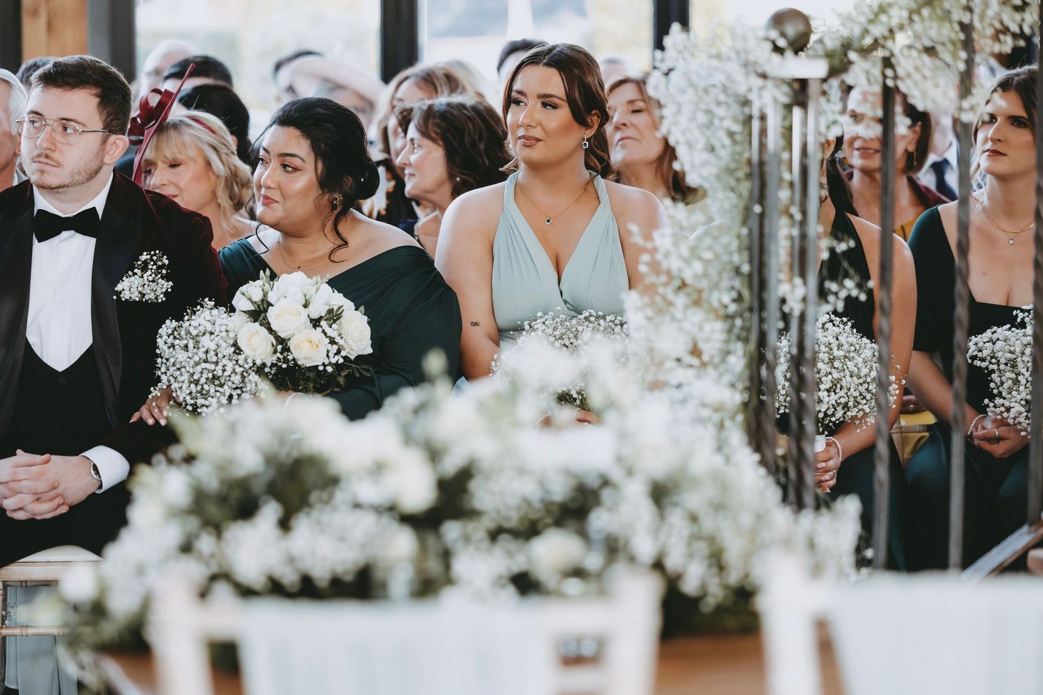 Wedding ceremony setup with white floral decorations and guests seated in elegant indoor venue.