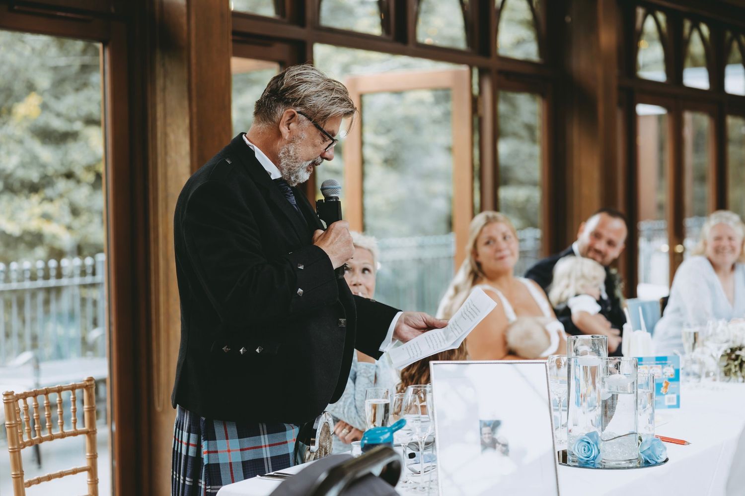 Wedding celebration in progress with guests seated at tables in rustic venue with wooden beams.
