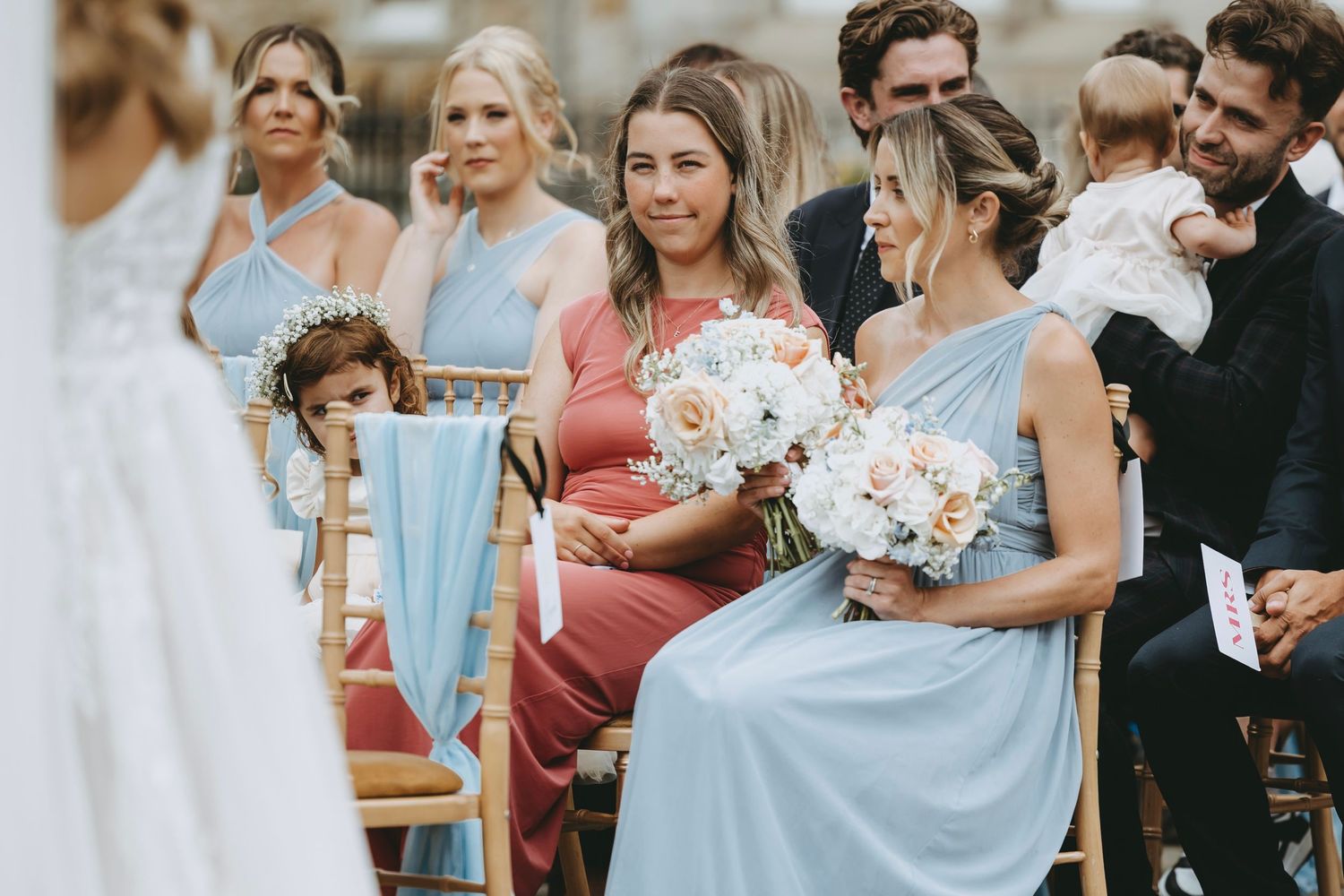 Wedding guests in pastel dresses gather during an outdoor celebration.